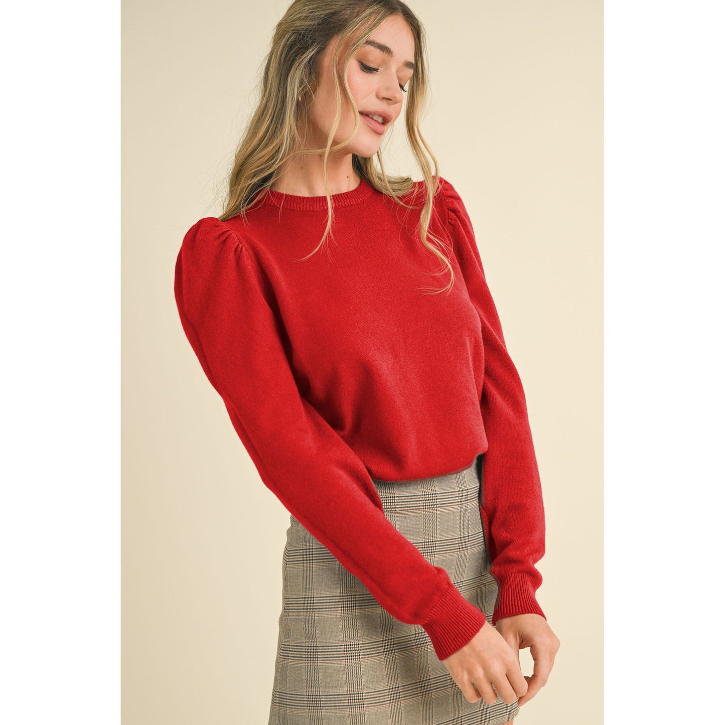 Woman wearing a red sweater with puff sleeves on a beige background