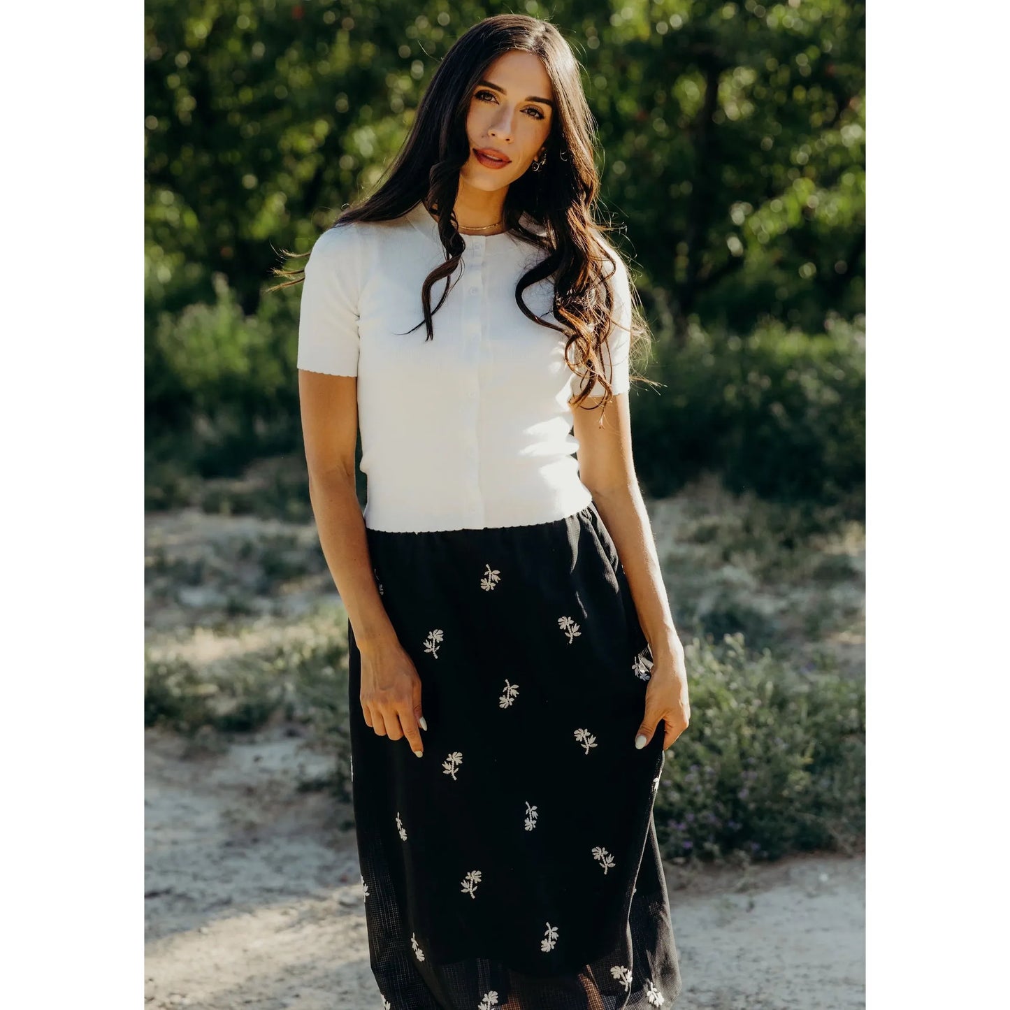 Woman wearing a white button down scalloped edge cardigan and skirt.