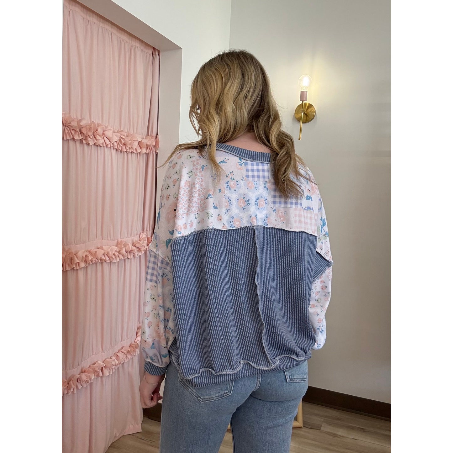 Person wearing a layered outfit with floral top and blue ribbed sweater in a room.