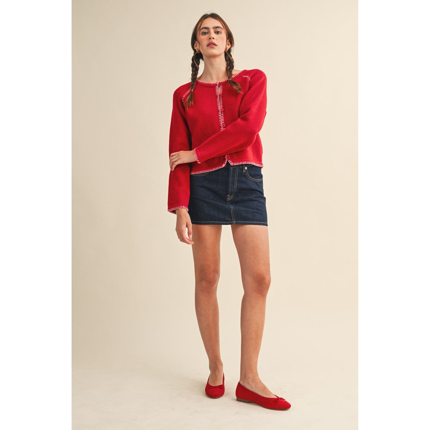 Woman wearing a red sweater and denim skirt on a beige background