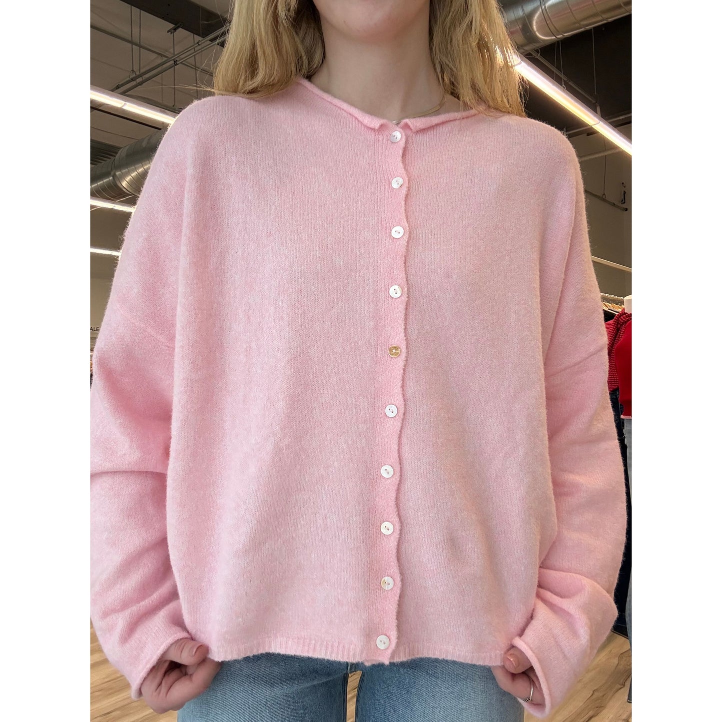 Pink garment with button details held by a person in an indoor setting