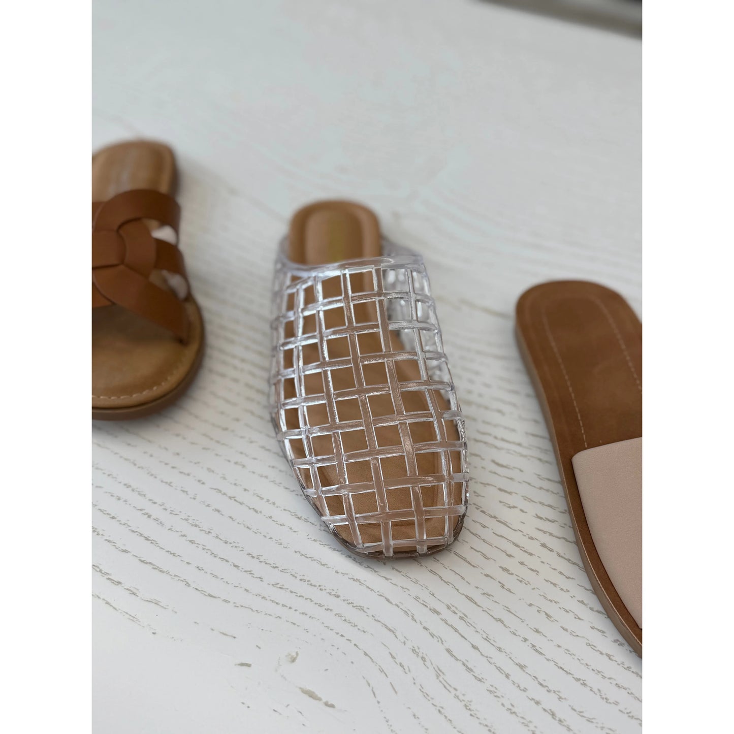 Clear woven sandal with brown sole on a textured white surface