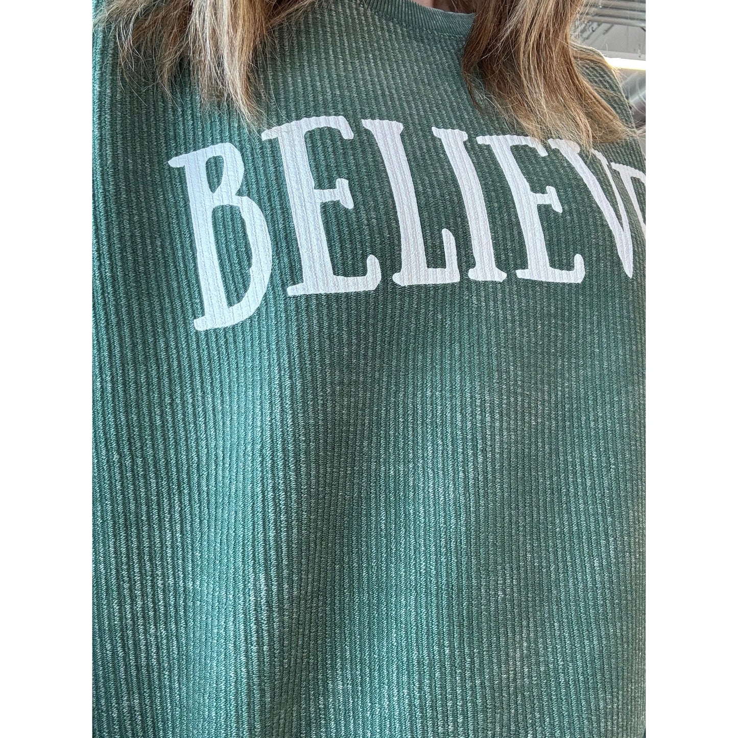 Green textured shirt with 'BELIEVE' text on a white background