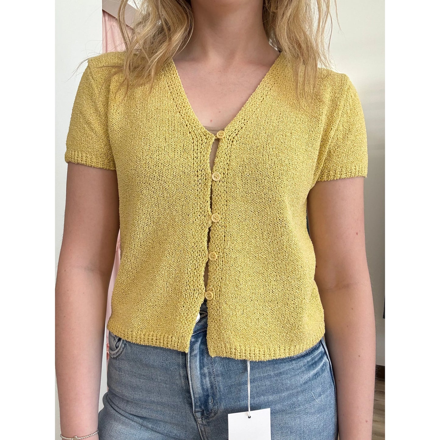 Person wearing a yellow knitted cardigan with a plain background