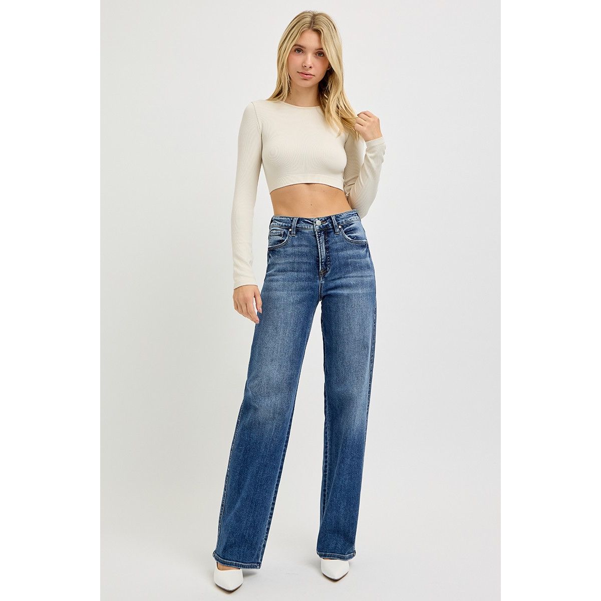 Woman wearing a white long-sleeve top and blue jeans on a white background