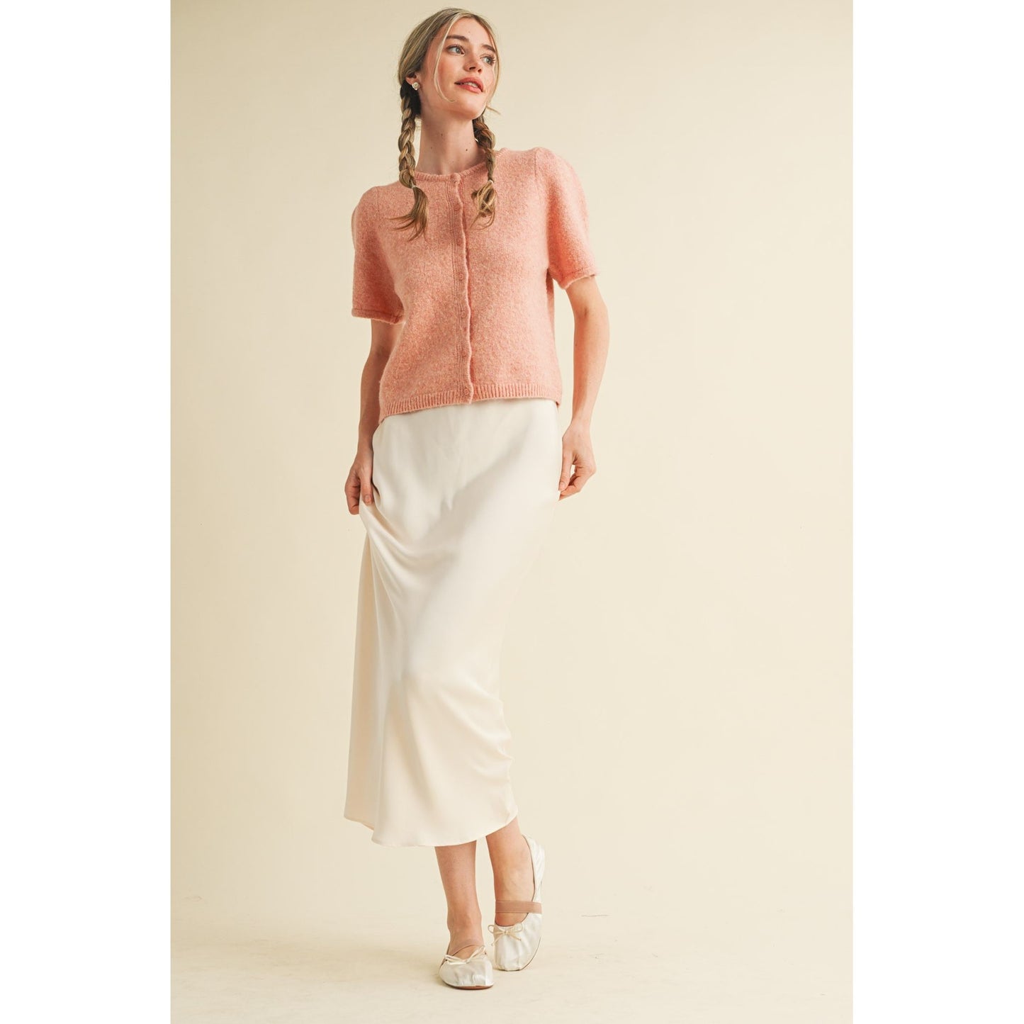 Woman wearing a pink knit top and white skirt on a beige background