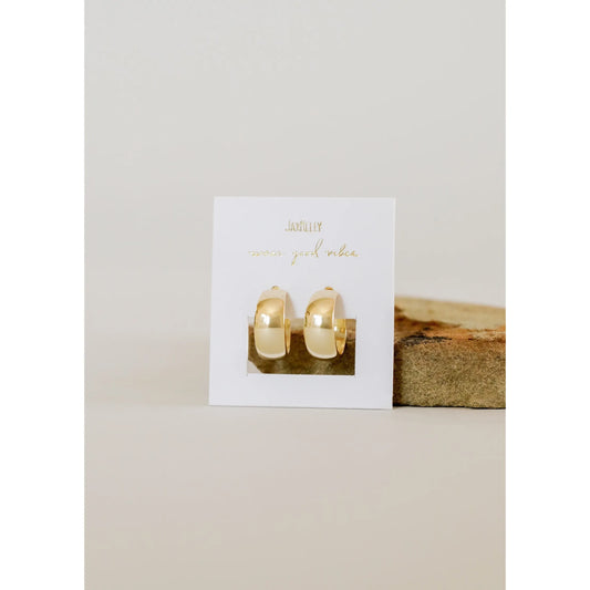 Gold hoop earrings on a white card with gold text, placed on a wooden block against a beige background.