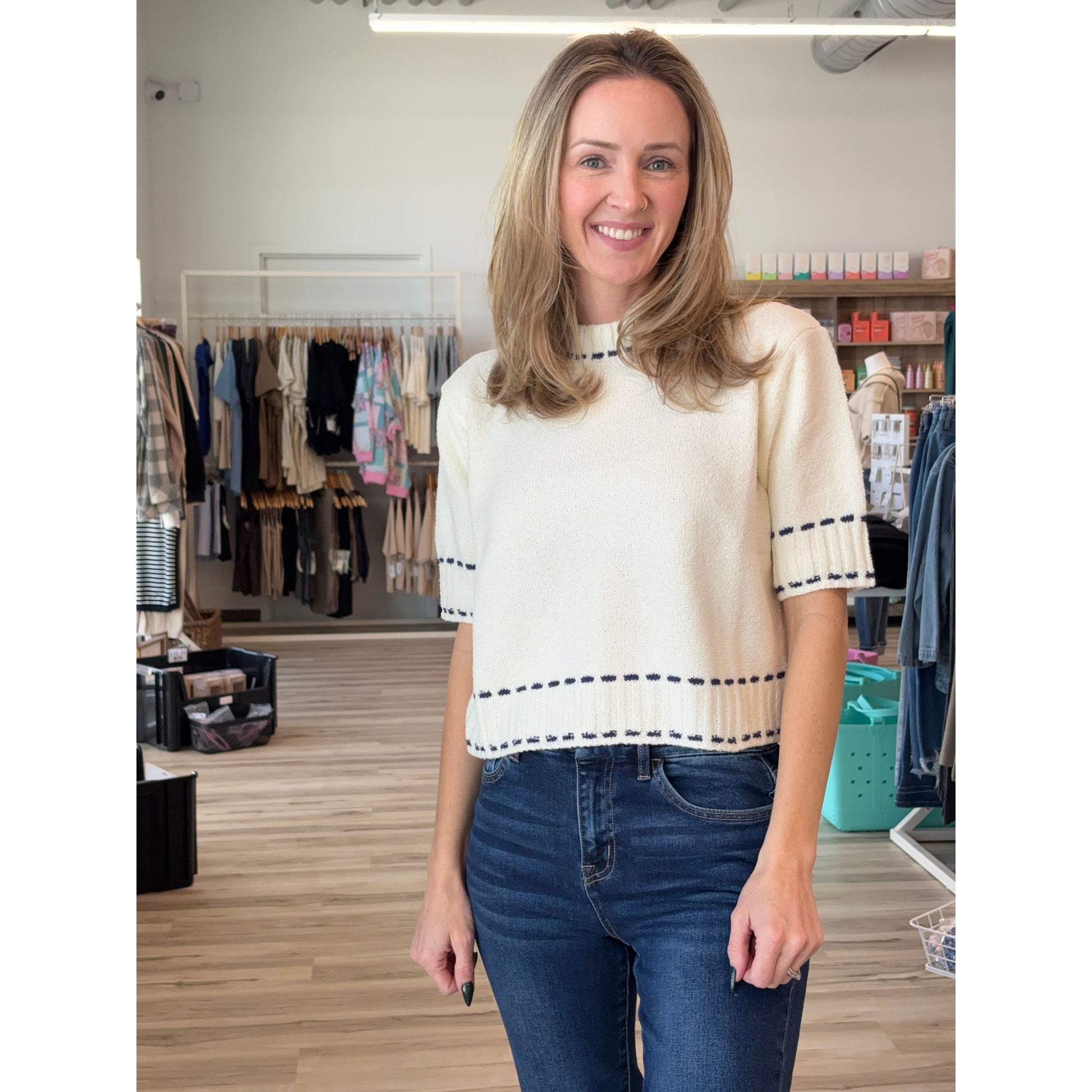 Woman wearing a cream-colored short-sleeved knit sweater with navy stitched detailing