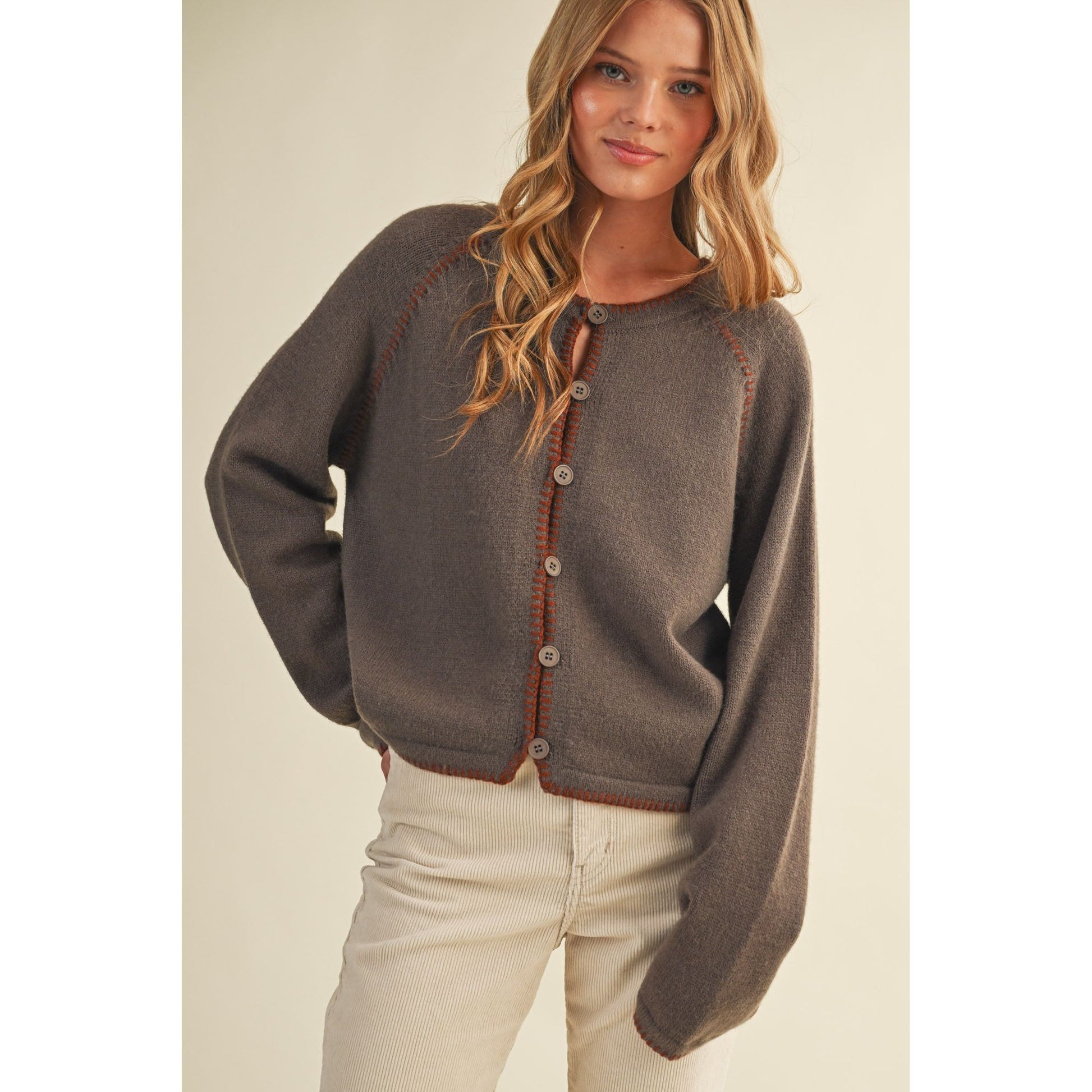 Woman wearing a brown cardigan with contrasting trim on a plain background