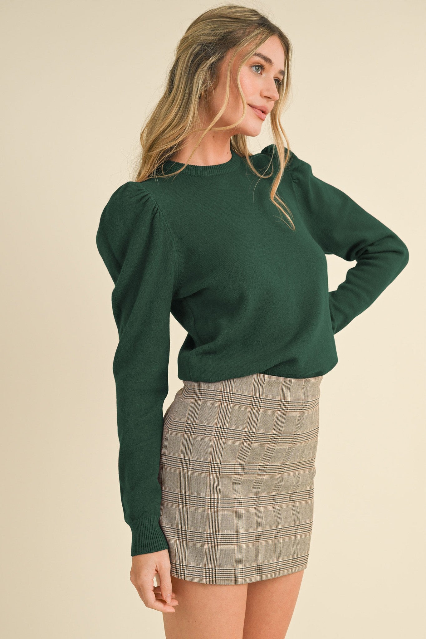 Woman wearing a green sweater and plaid skirt against a beige background