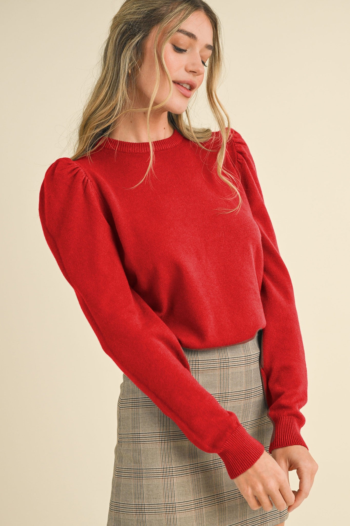 Woman wearing a red sweater with puff sleeves on a beige background