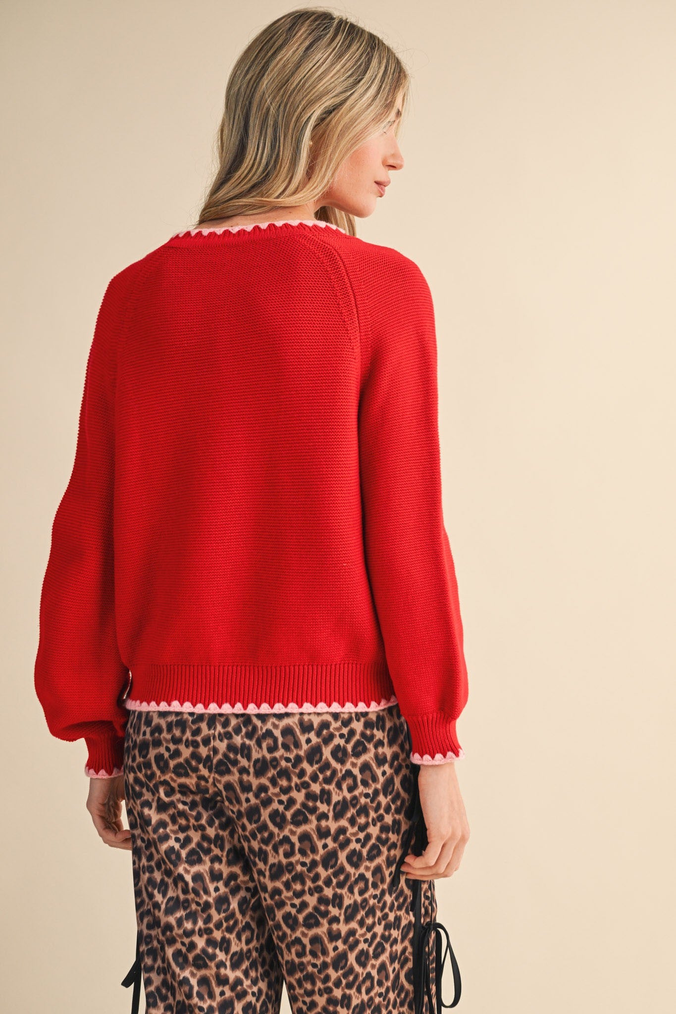 Person wearing a red sweater and leopard print pants on a beige background
