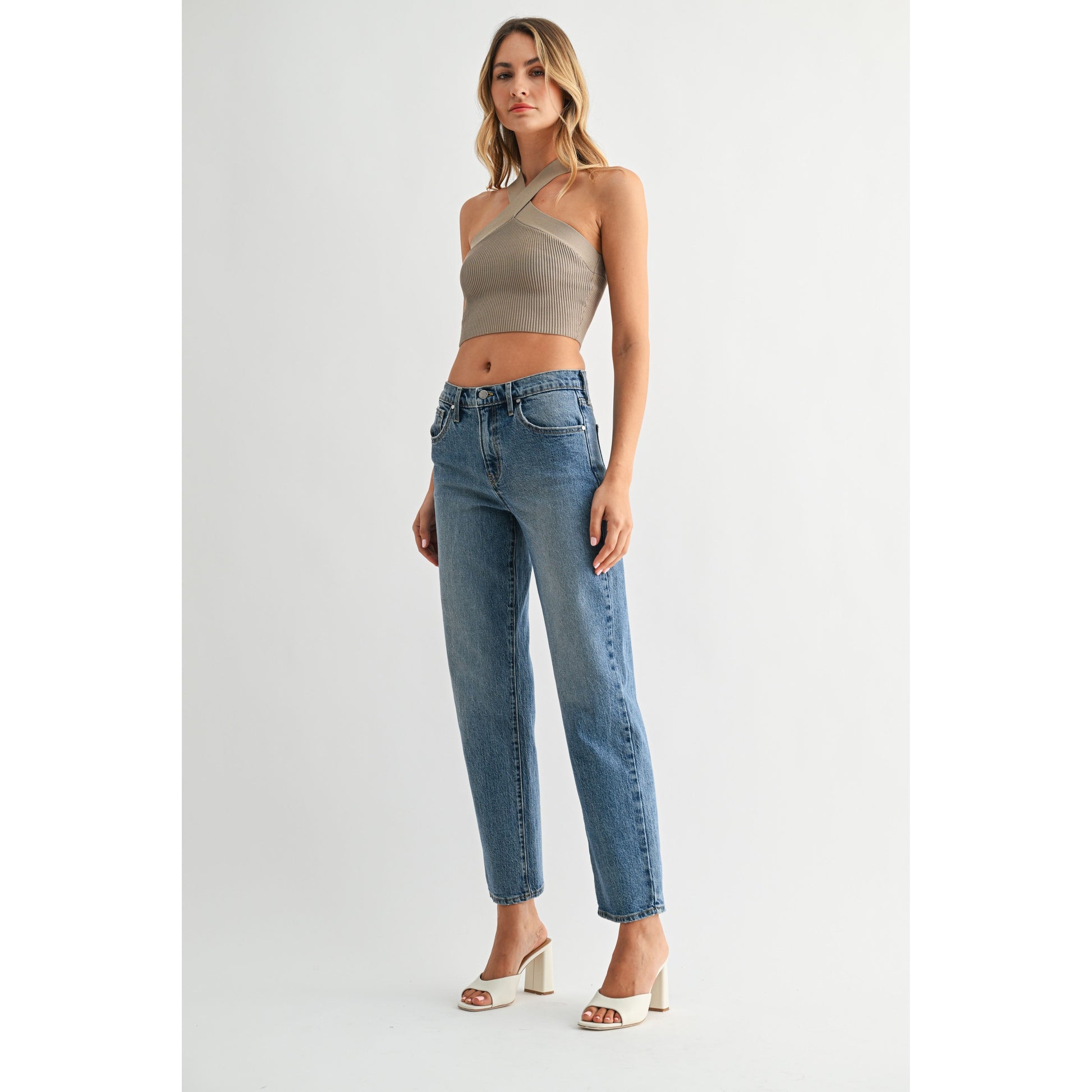 Woman wearing a beige halter top and blue jeans on a white background