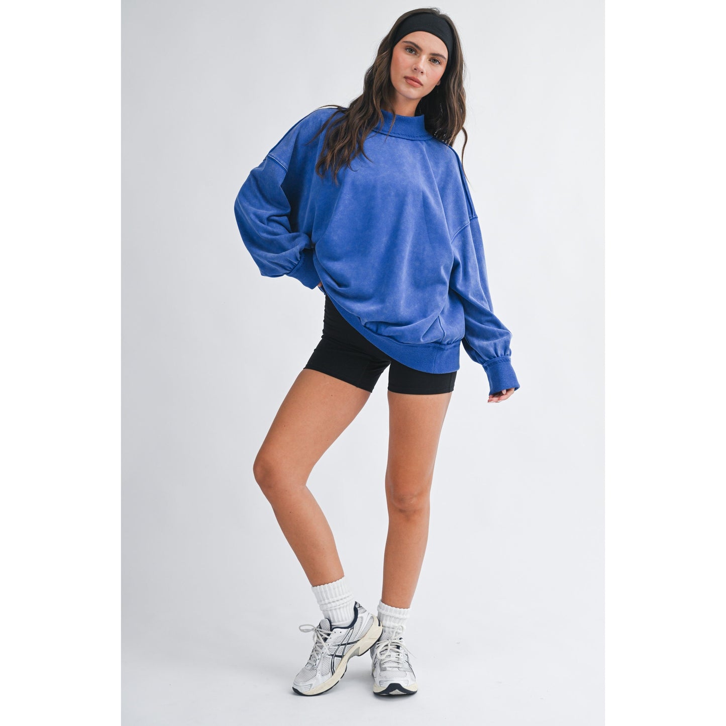 Person wearing a blue oversized sweatshirt, black shorts, and white sneakers on a white background