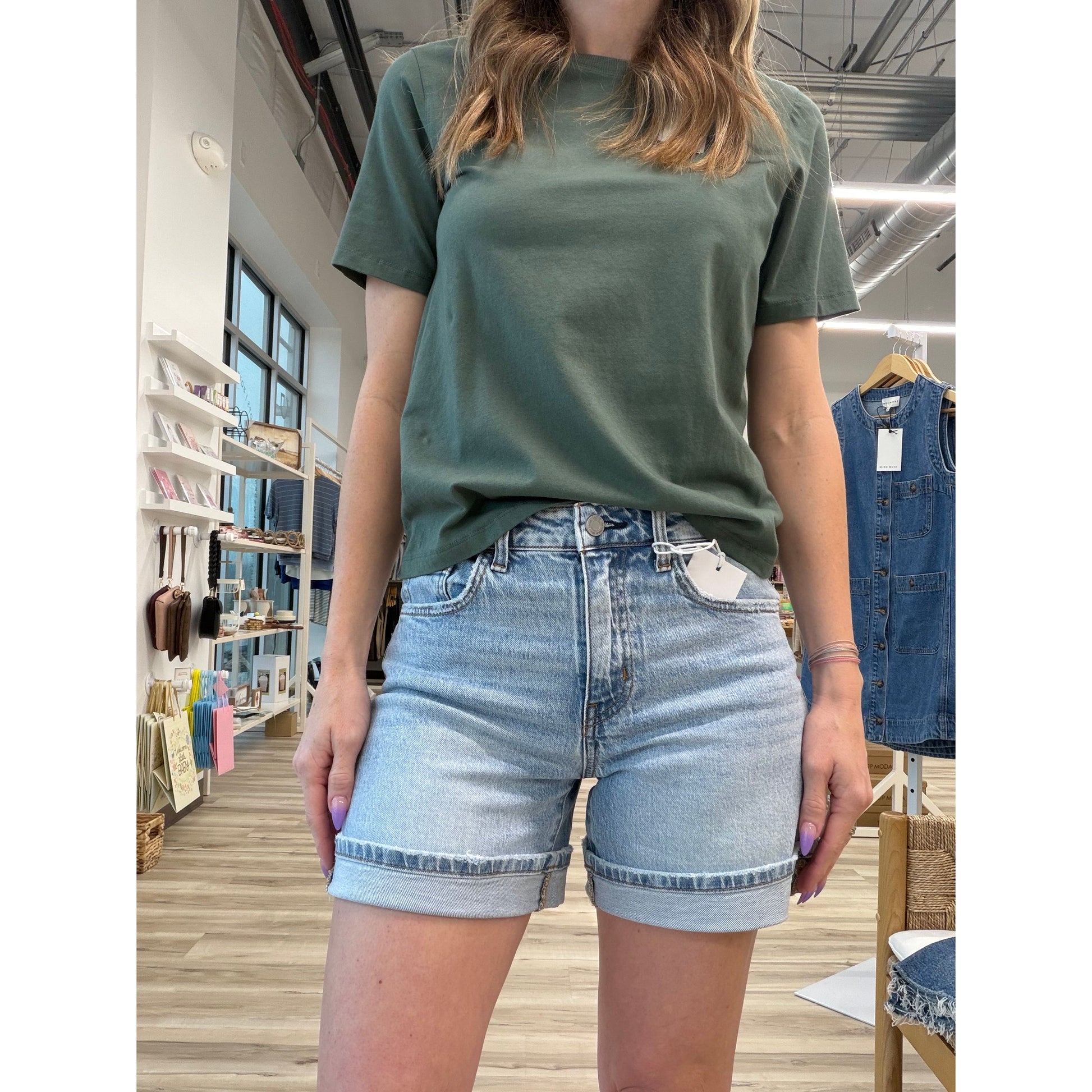 Person wearing a green t-shirt and light wash denim shorts with a cuff in a store setting