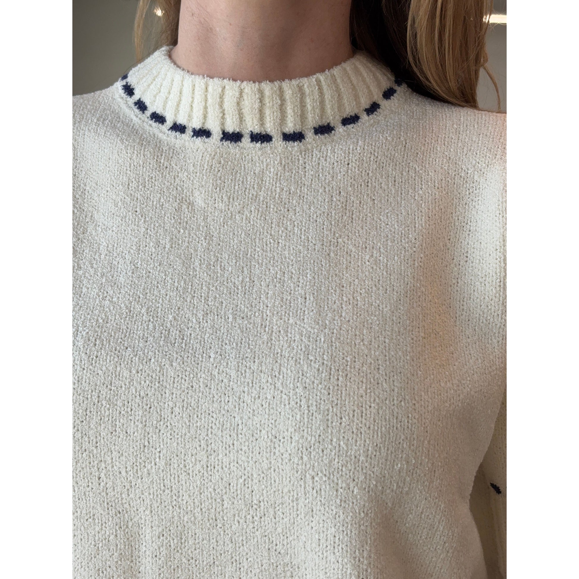 Close-up of a woman wearing a cream knit sweater with navy stitch detailing on the collar