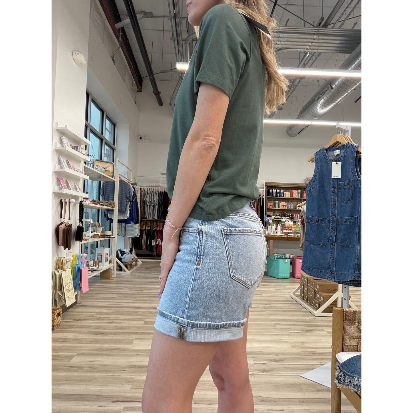 Person wearing a green t-shirt and light wash denim shorts with a cuff in a store setting
