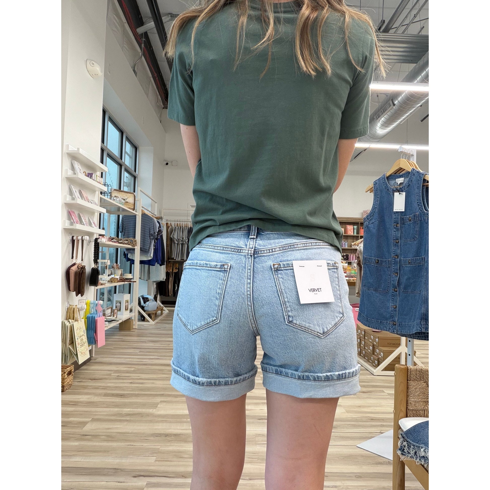 Person wearing a green t-shirt and light wash denim shorts with a cuff in a store setting
