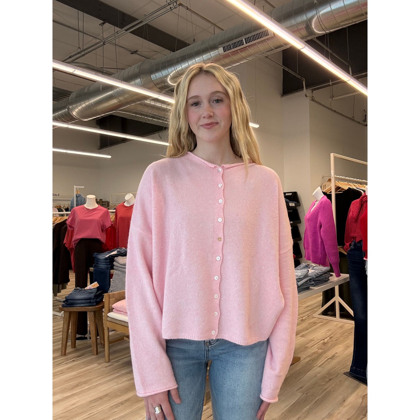 Person wearing a pink cardigan in a store setting with clothing racks and displays.
