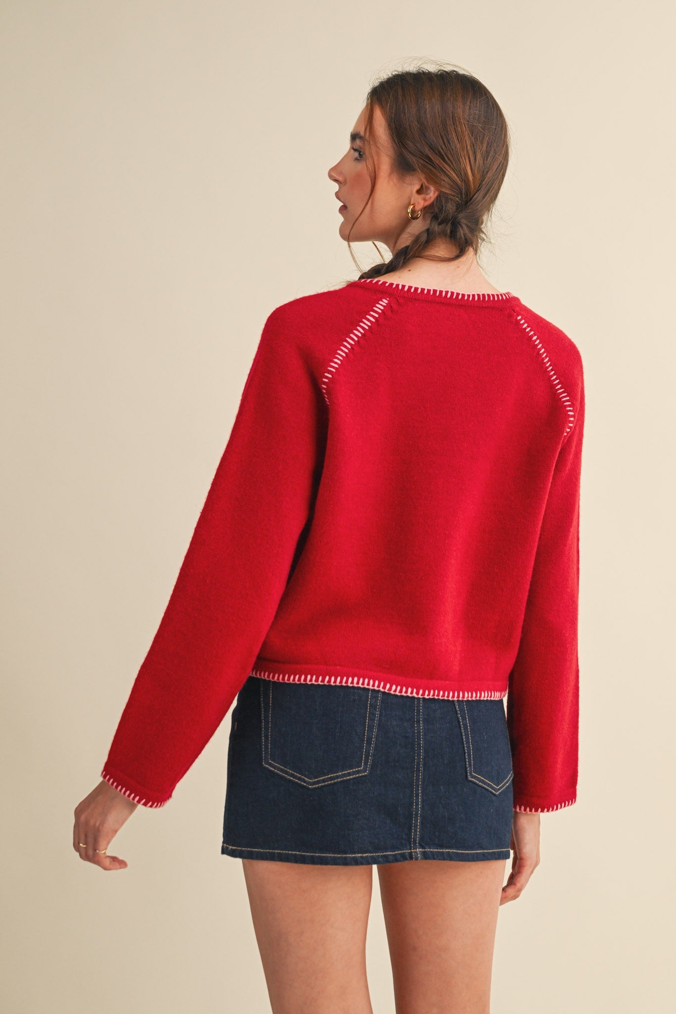 Woman wearing a red sweater with white trim on a beige background