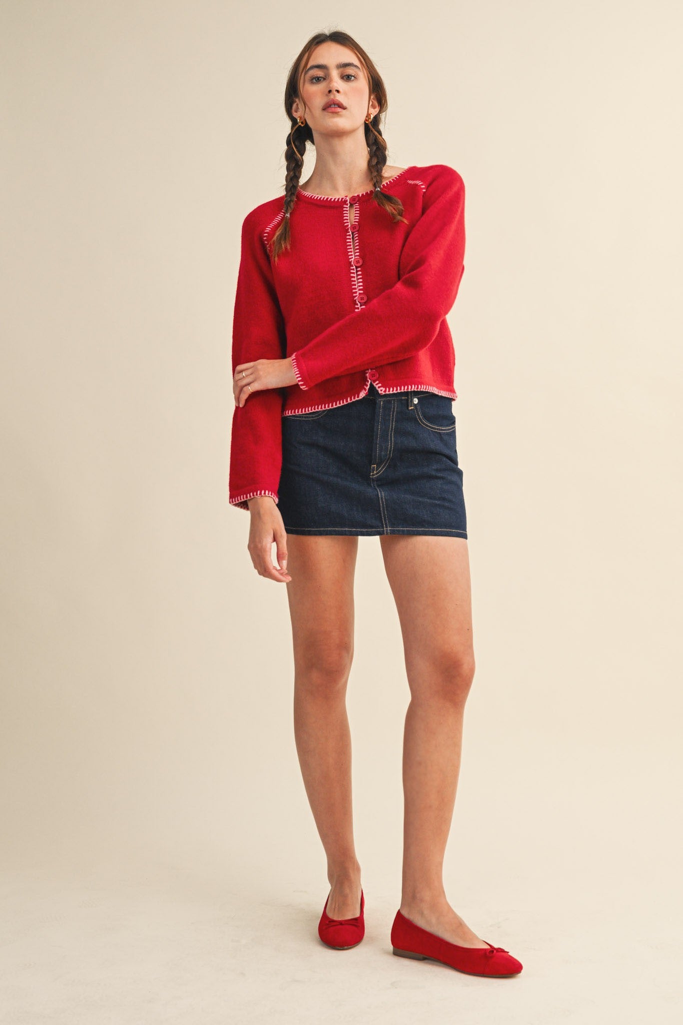 Woman wearing a red sweater and denim skirt on a beige background