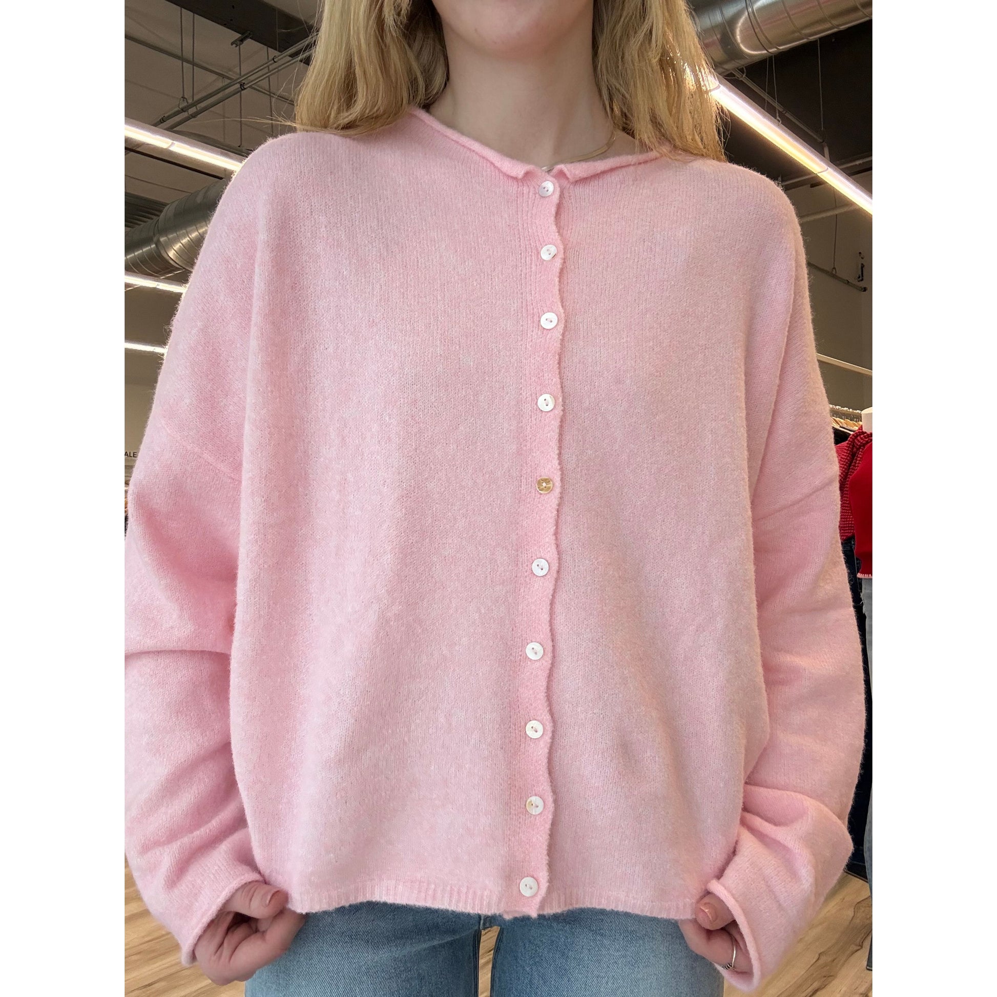 Pink garment with button details held by a person in an indoor setting