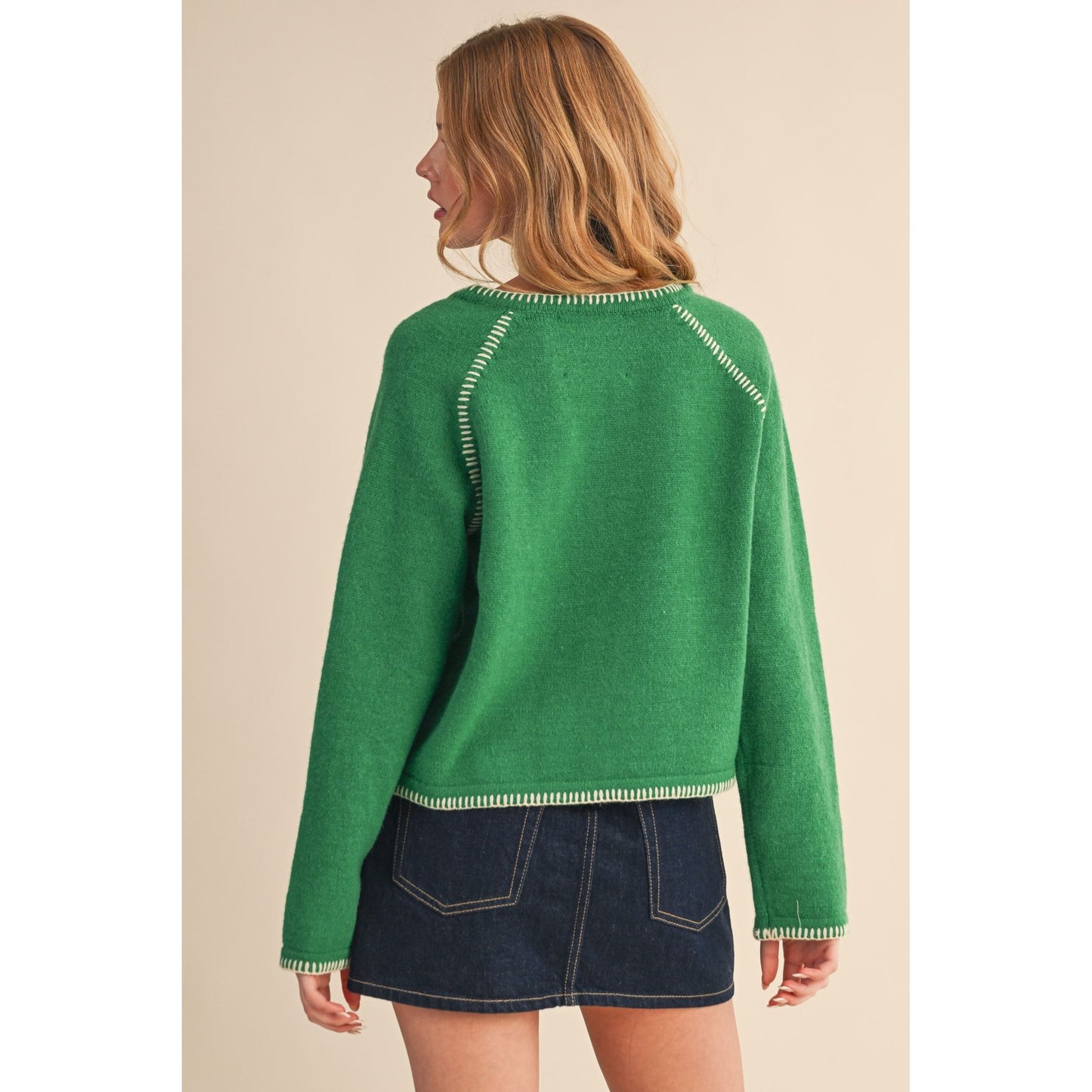 Woman wearing a green sweater with white trim on a beige background