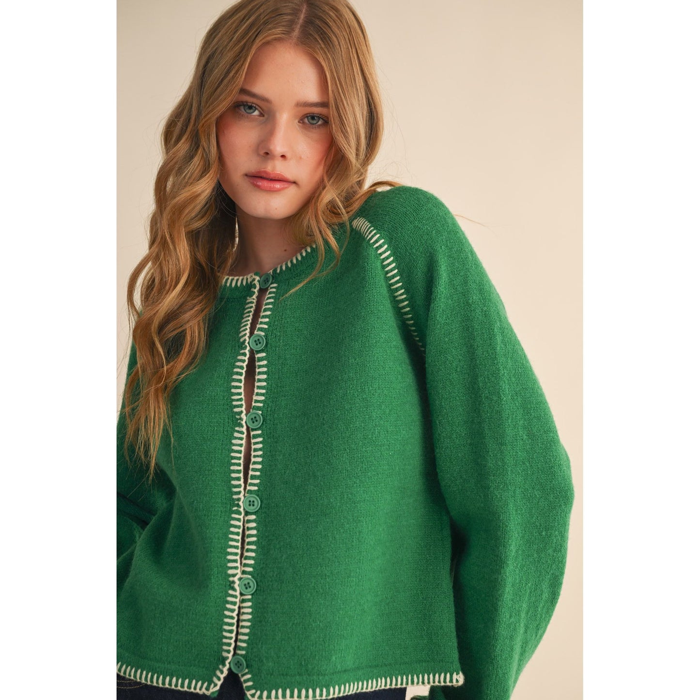 Woman wearing a green sweater with white trim against a beige background