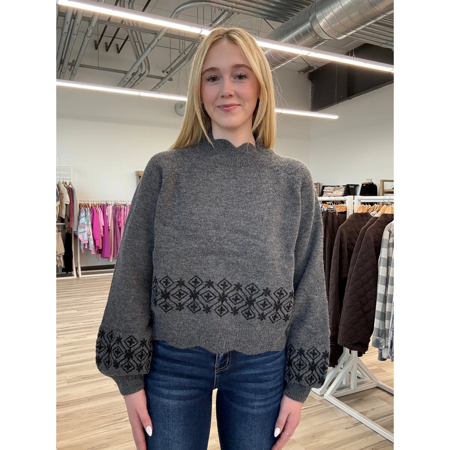 Person wearing a gray sweater with an embroidered pattern in a clothing store