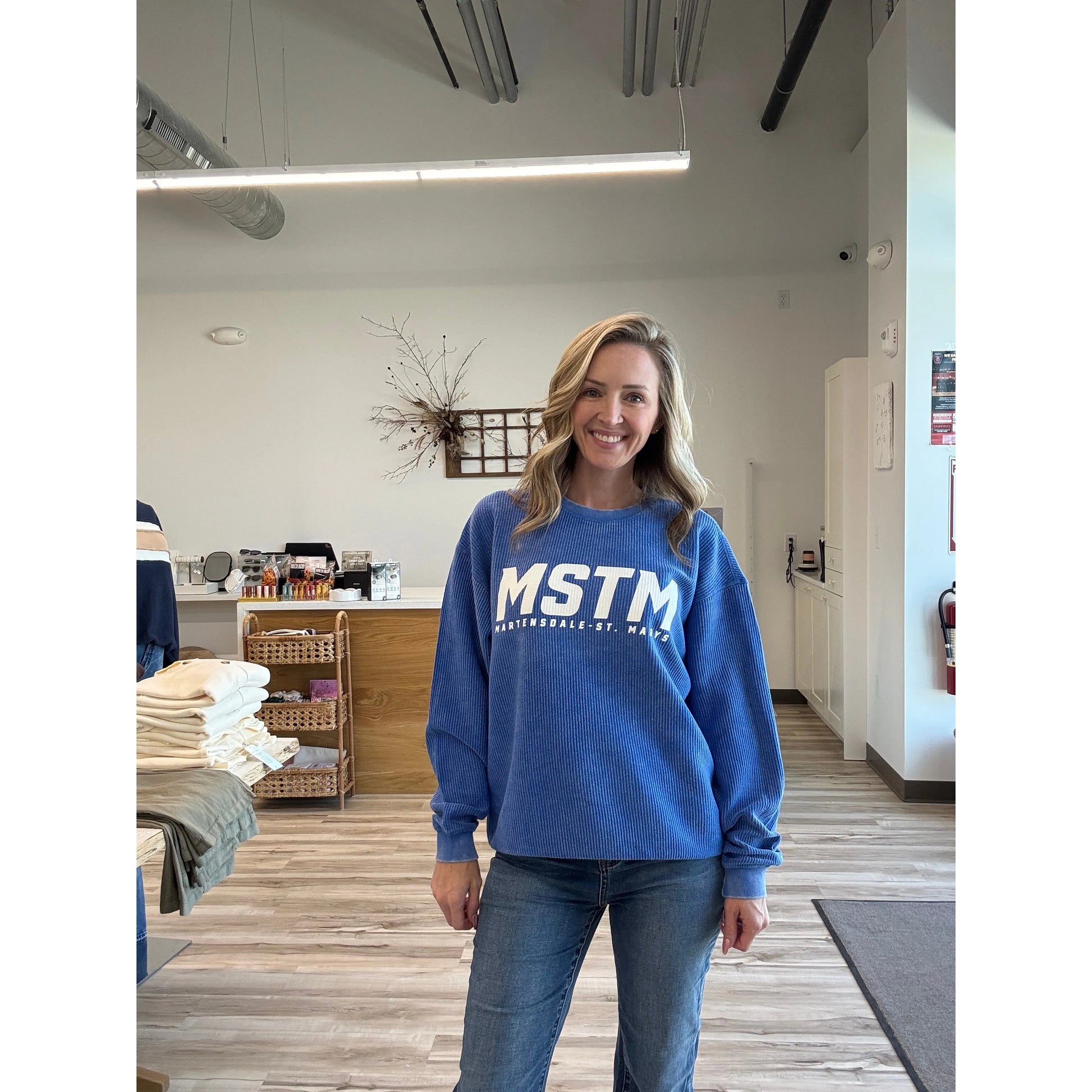 Woman wearing a blue sweatshirt with 'MSTM' text in an indoor setting