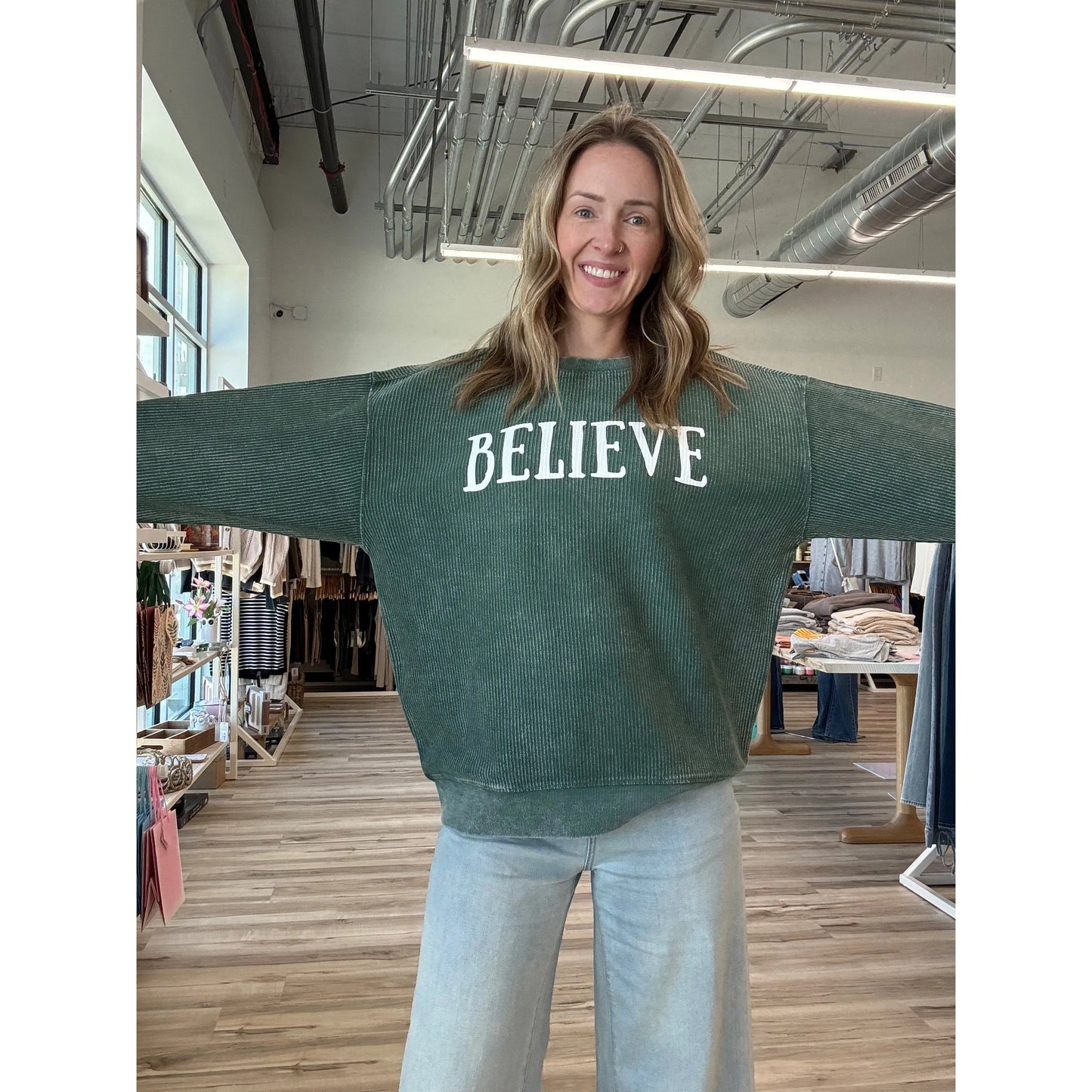 Person wearing a green sweater with 'BELIEVE' text in a store setting