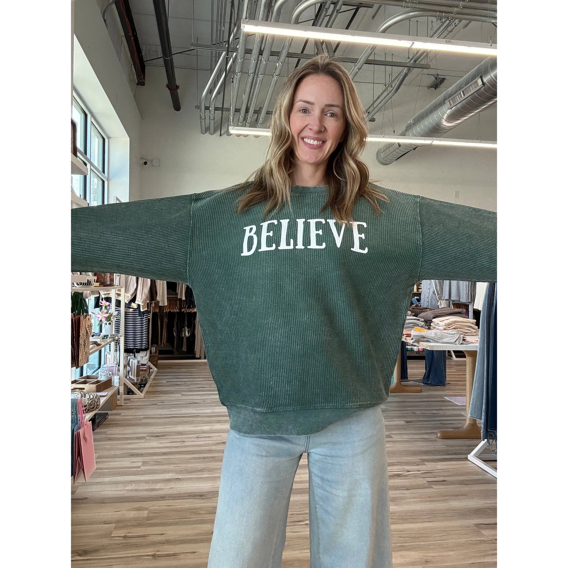Person wearing a green sweater with 'BELIEVE' text in a store setting