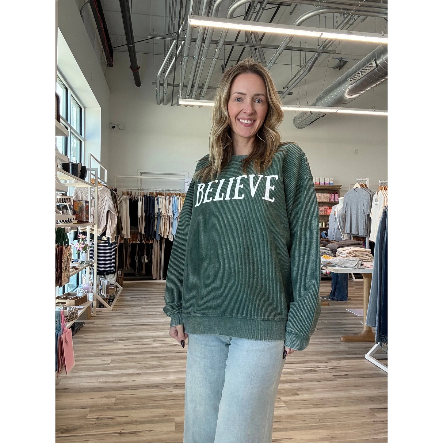 Woman wearing a green sweatshirt with 'BELIEVE' text in a store setting