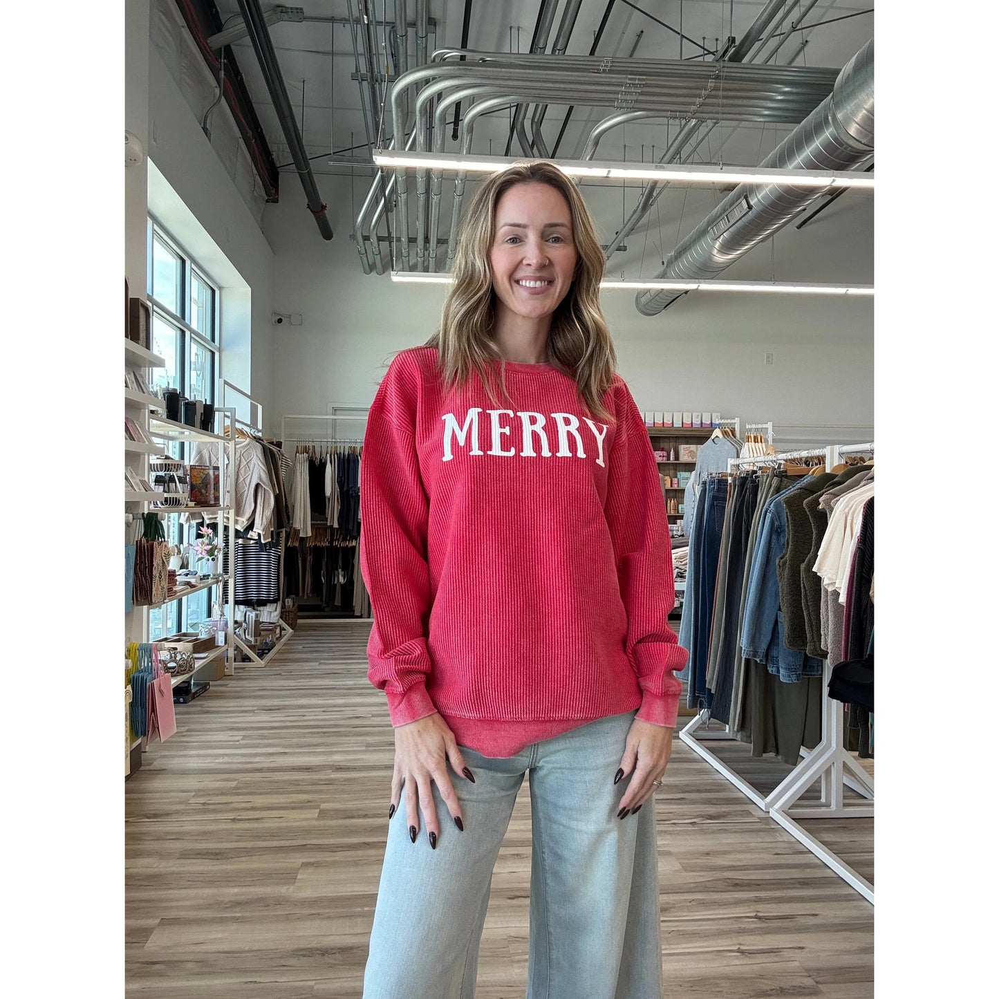 Woman wearing a red 'MERRY' sweater in a store setting