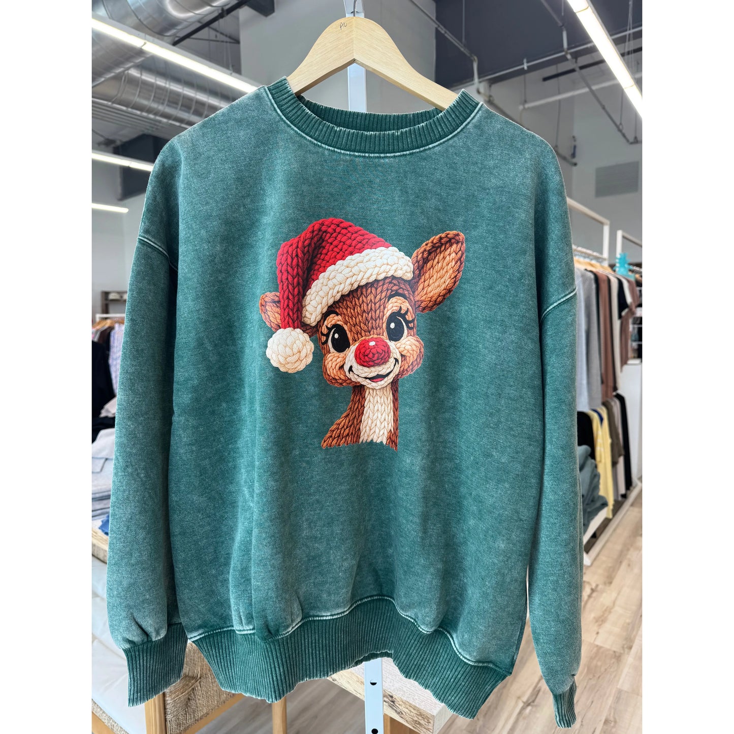 Green sweater with a reindeer design on a hanger in a store setting