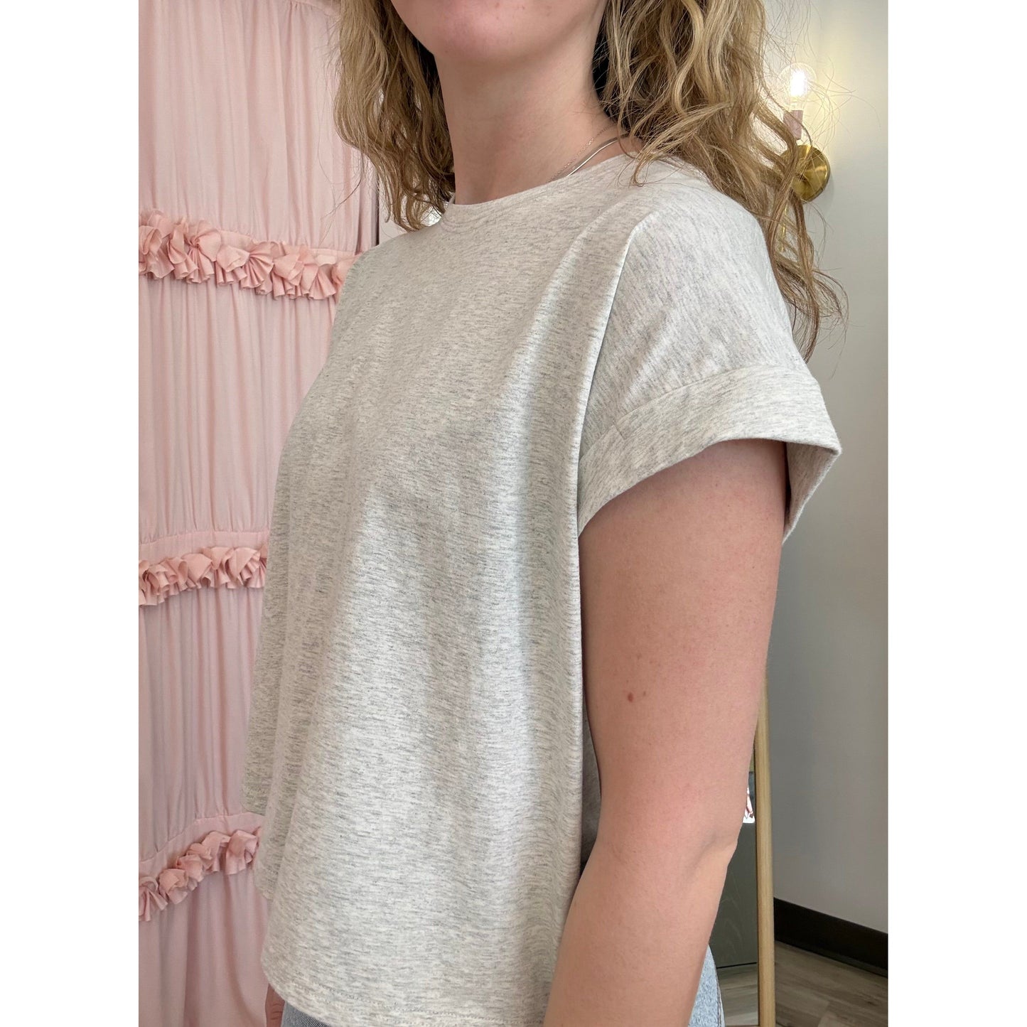Person wearing a light gray t-shirt in a room with pink decorative elements.
