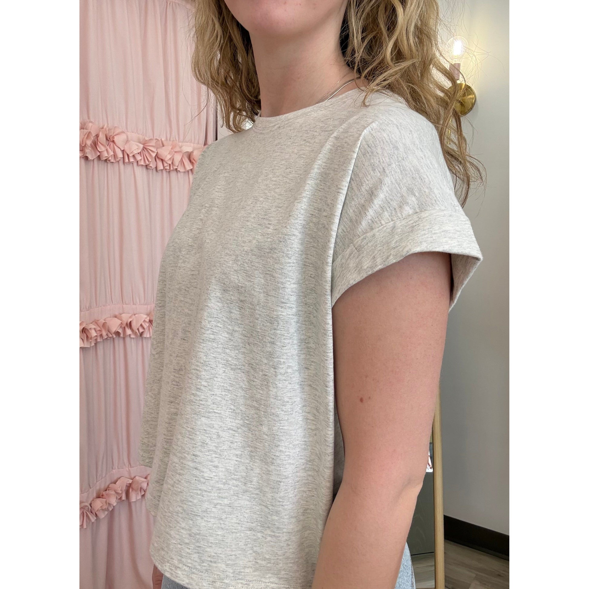 Person wearing a light gray t-shirt in a room with pink decorative elements.