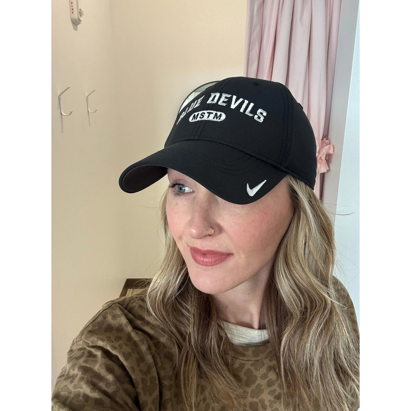 Person wearing a Nike black cap with 'Devils' and 'MSTM' text, indoors.