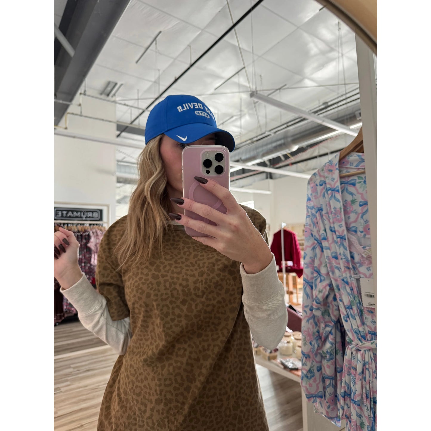 Person taking a mirror selfie wearing a blue Nike hat in a store