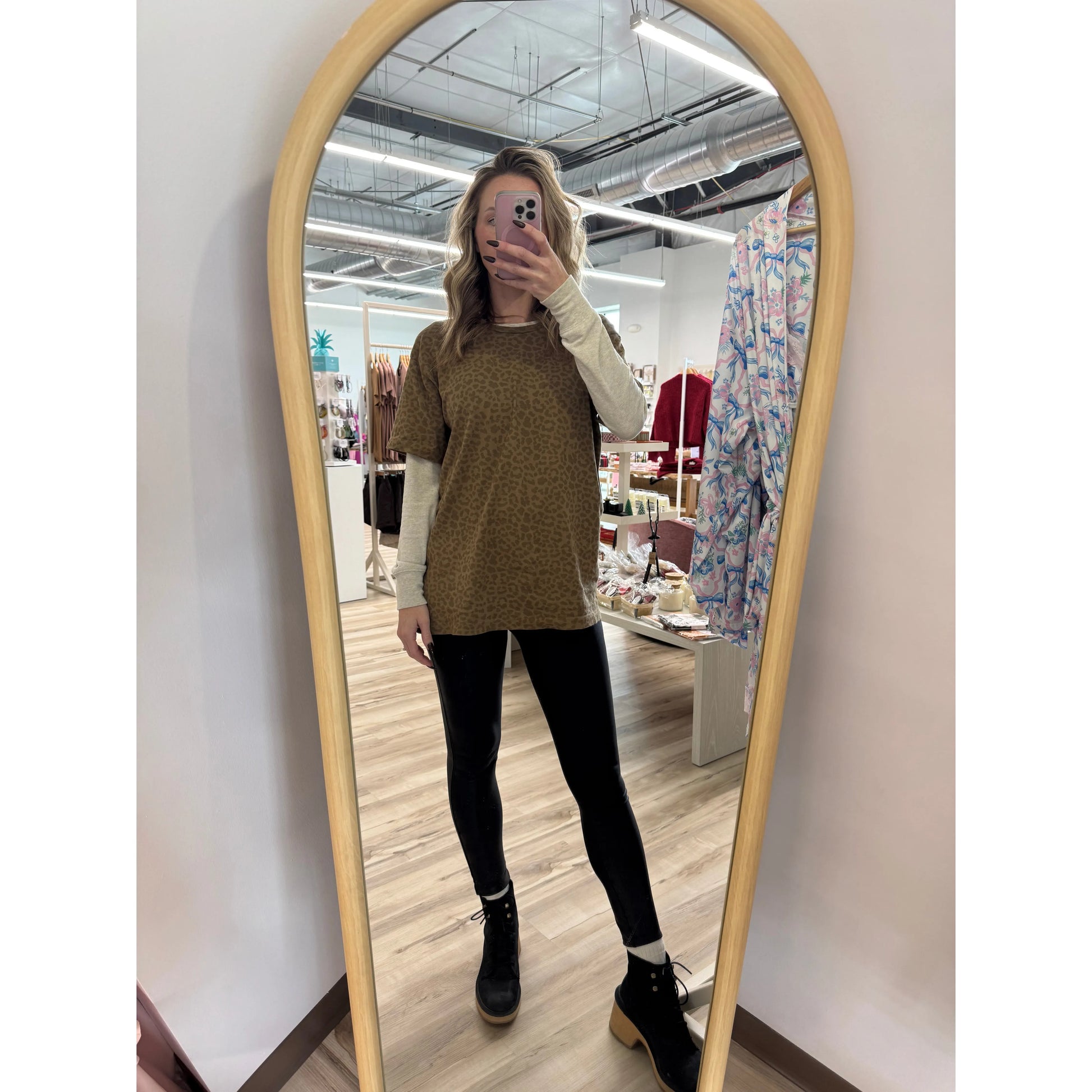 Person taking a mirror selfie wearing a brown leopard shirt and black pants in a store.