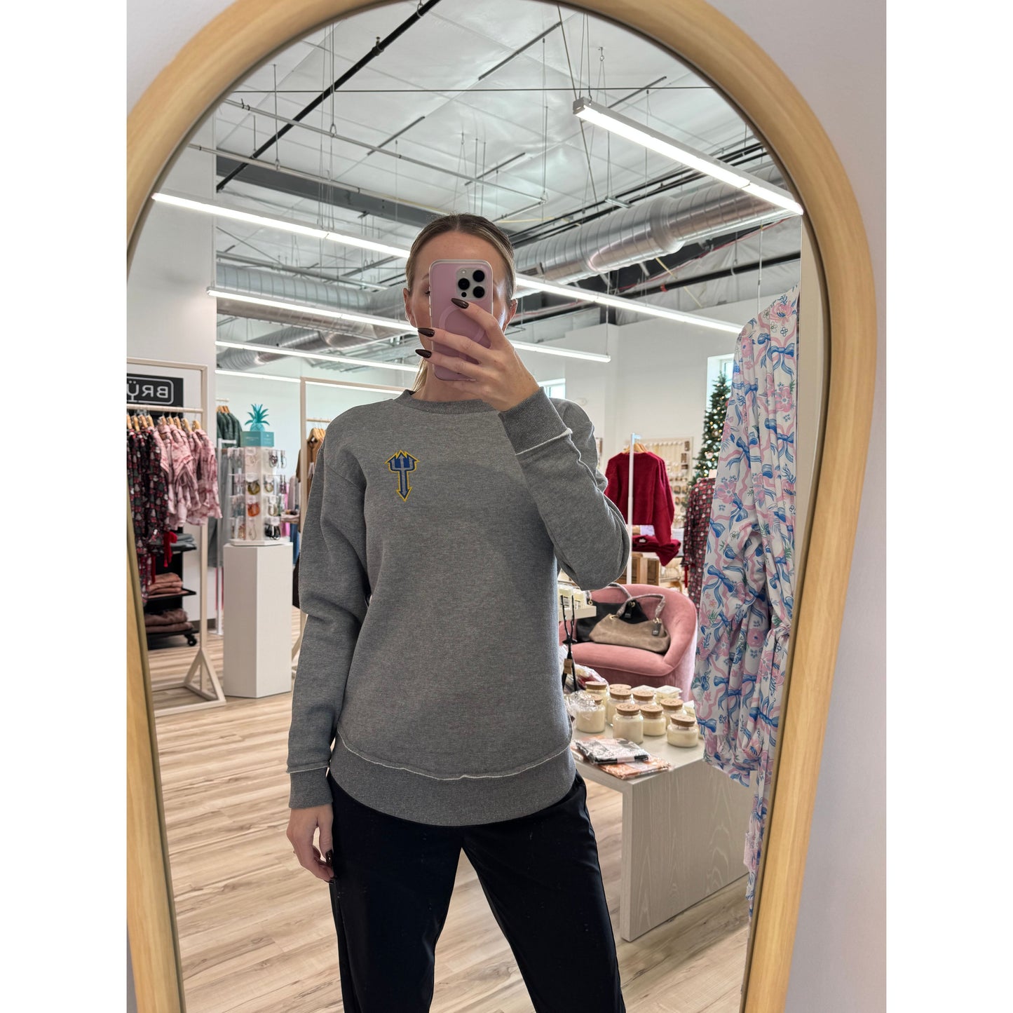 Person wearing a gray sweatshirt with a logo in a store setting, taking a mirror selfie.