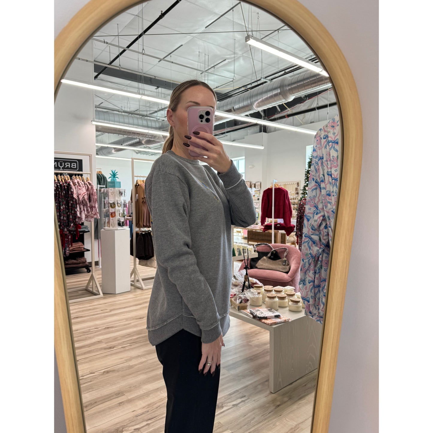 Person taking a mirror selfie in a store wearing a grey sweatshirt 