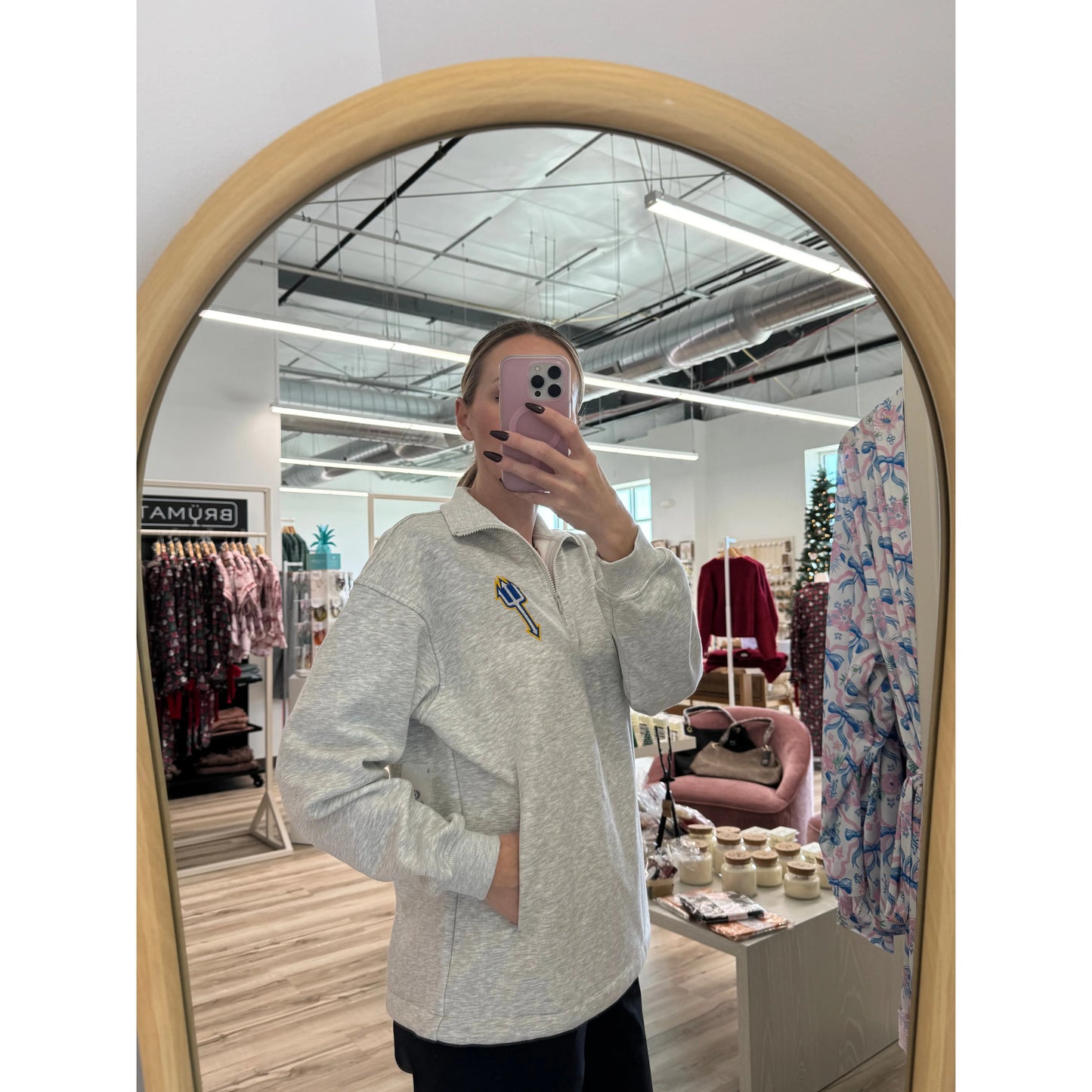 Person taking a mirror selfie wearing a light gray sweater in a store setting.