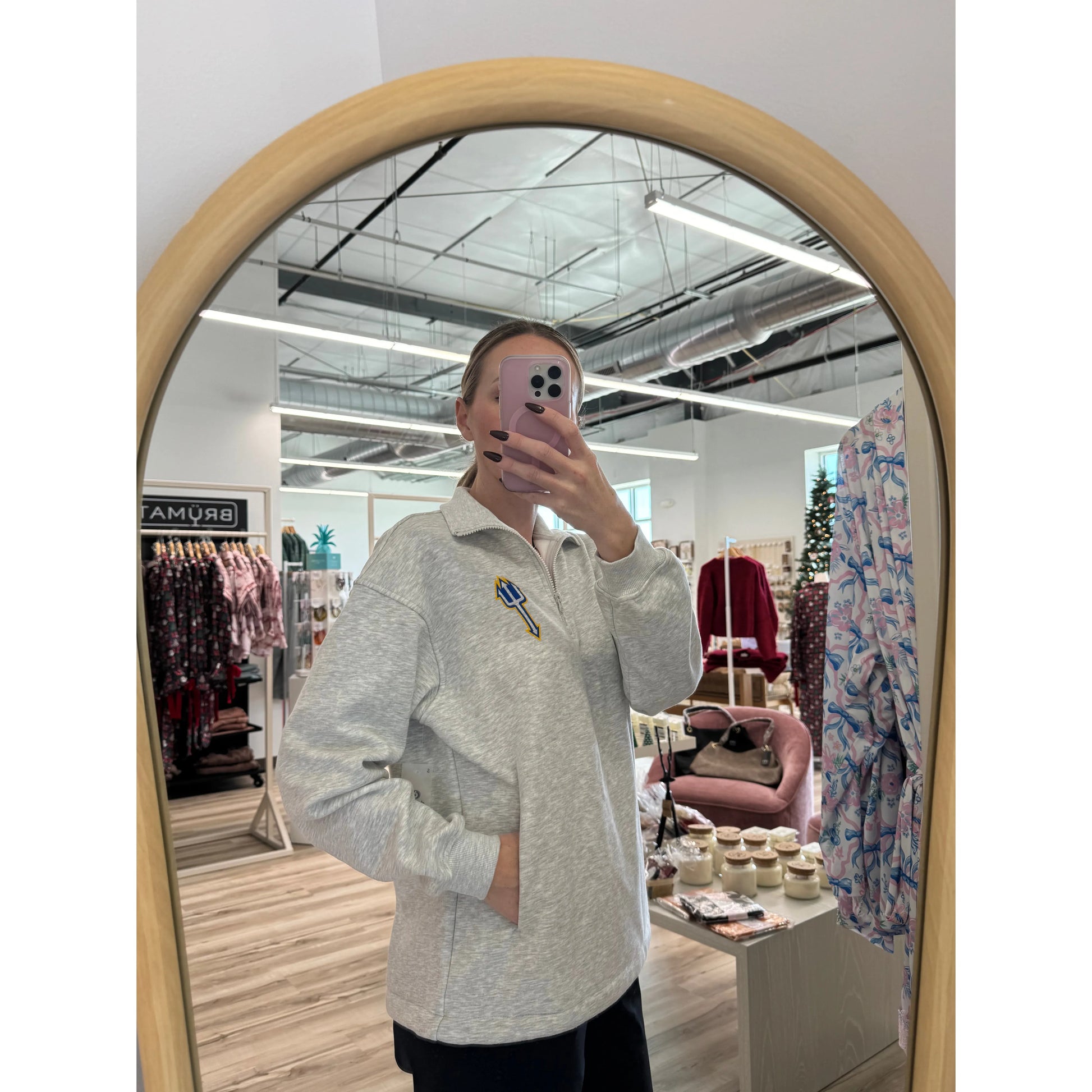 Person taking a mirror selfie wearing a light gray sweater in a store setting.