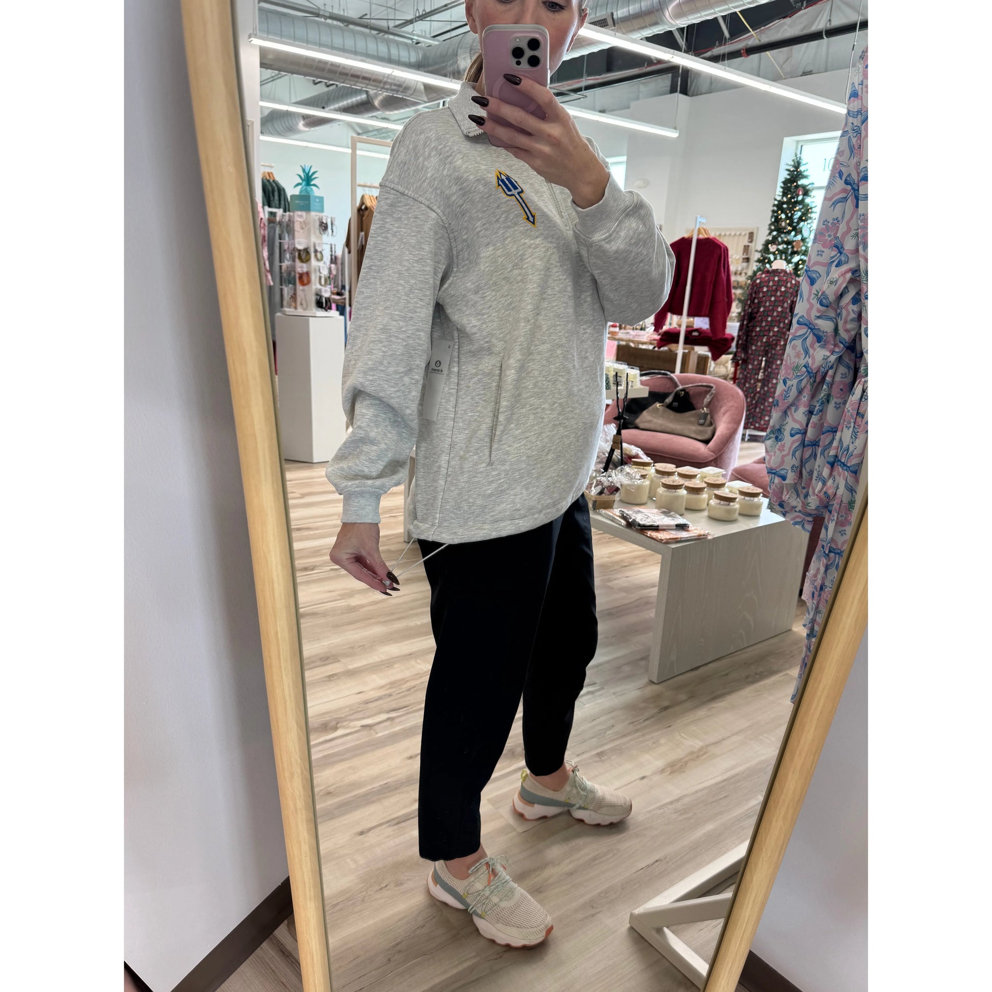 Person taking a mirror selfie wearing a gray sweatshirt and black pants in a store.