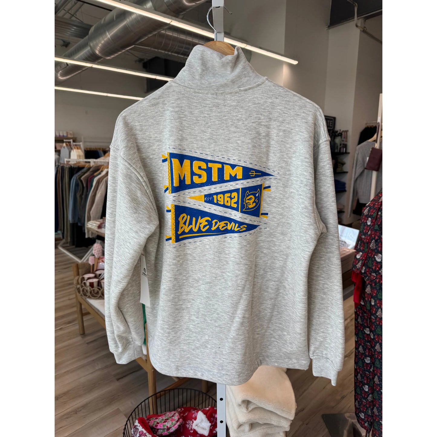Gray sweatshirt with 'MSTM Blue Devils' design hanging in a store.