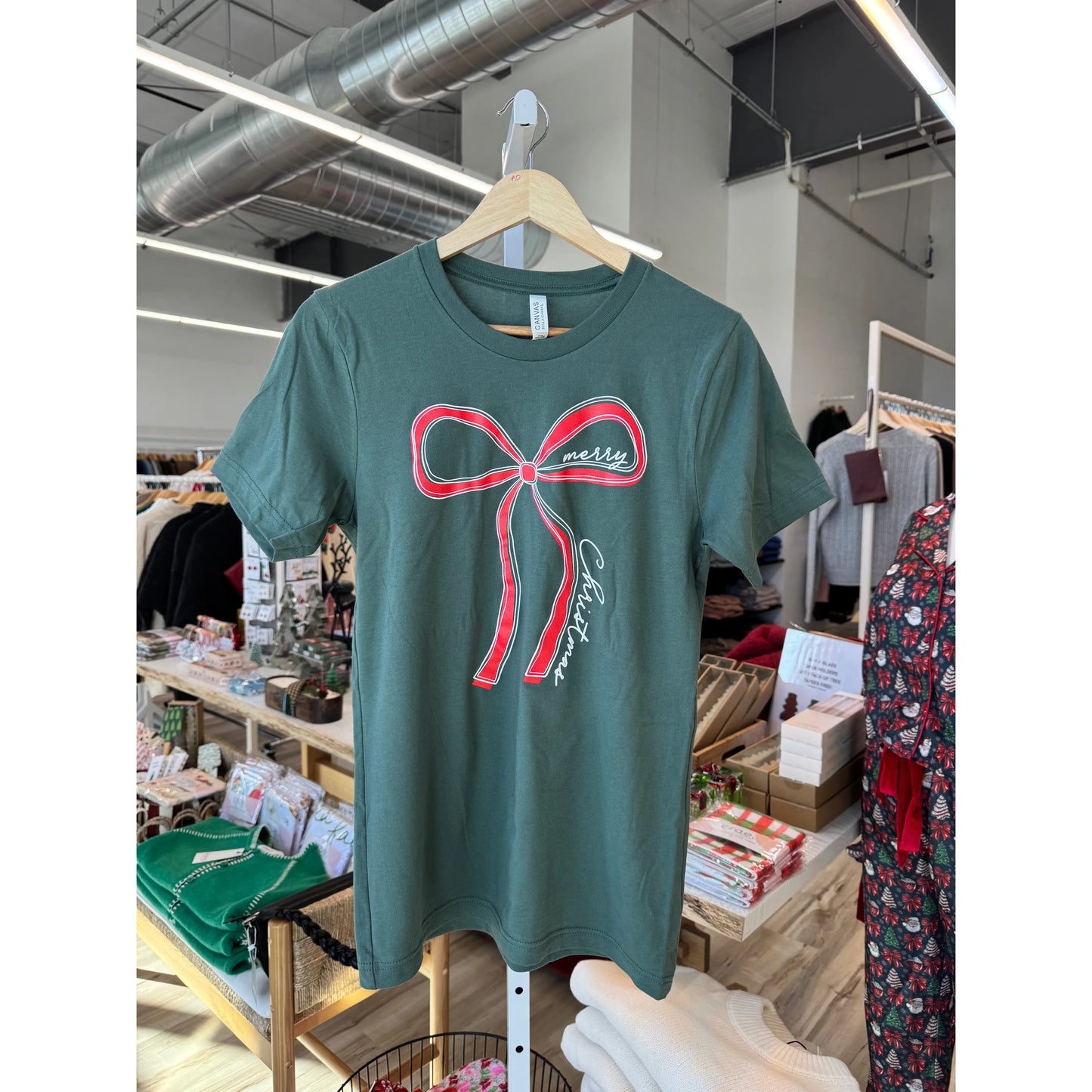 Green t-shirt with a red bow design on a hanger in a store setting