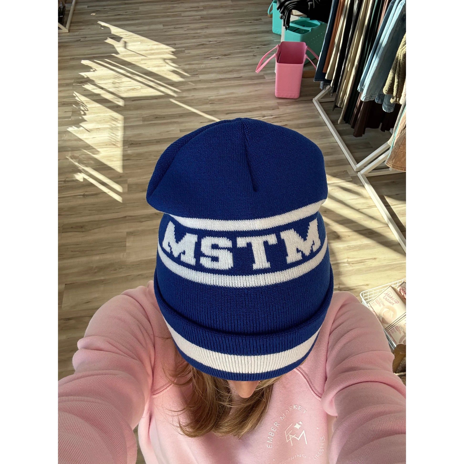 Person wearing a blue beanie with 'MSTM' on it in a store setting