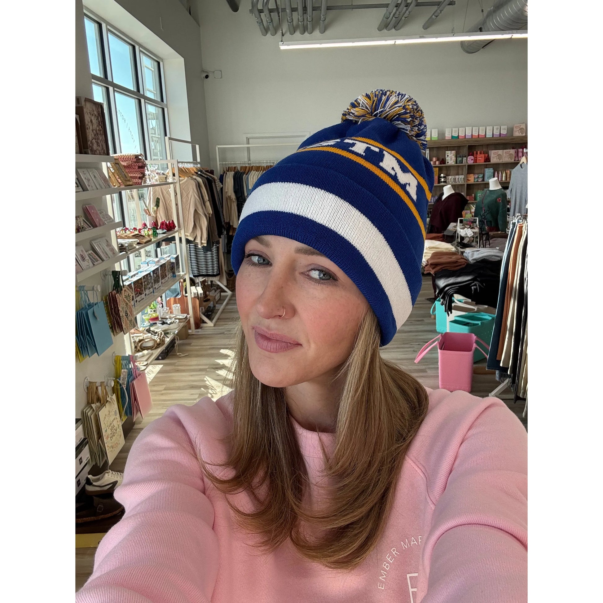 Woman wearing a blue and white beanie with a 'MSTM' logo, in a store setting.