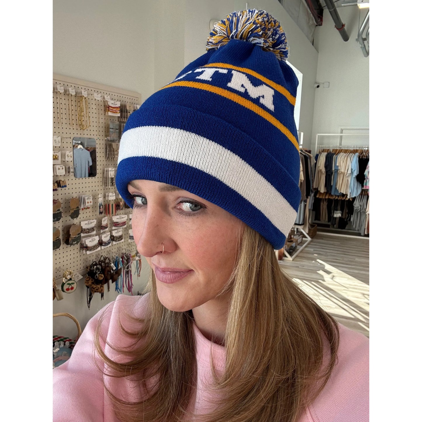 Woman wearing a blue knit beanie with pom-pom with a logo in a store setting